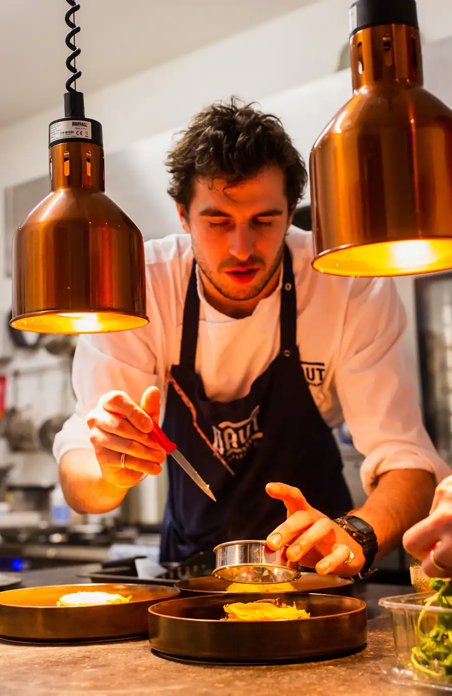 A chef finishing plates under copper pass lights